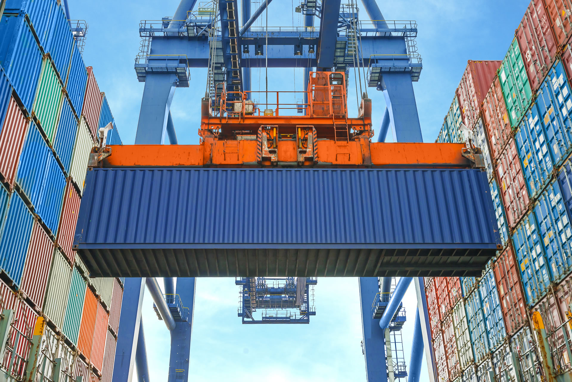 High-angle view of a massive container ship's bow, fully loaded with multi-colored cargo boxes, docked at a port terminal with cranes visible on the side